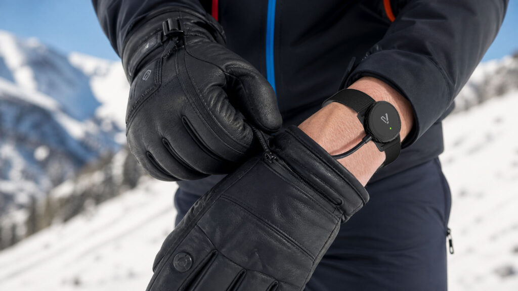 Skier pulling on a black glove with the IASUS BLE In Glove PTT module on the wrist and wire running to the fingertip